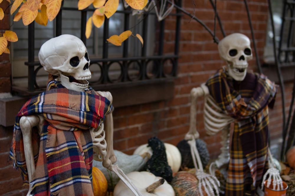 Halloween skeleton decorations wearing scarves in front of a brick home during autumn in New York City